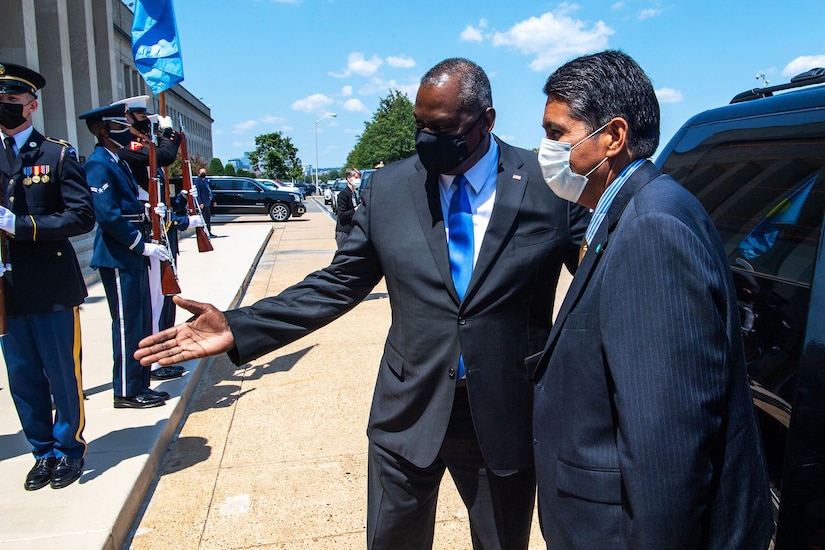Two men stand next to a a car as others stand around.