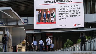 Pedestrians walk past a big screen displaying news about the Quad Leaders’ Summit, Tokyo, May 2022